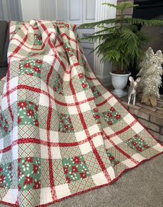 a red and white quilt sitting on top of a floor next to a potted plant