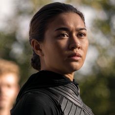 a close up of a person wearing a black shirt and looking at the camera with trees in the background