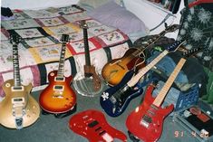 guitars are lined up on the floor in front of a quilted bedspread