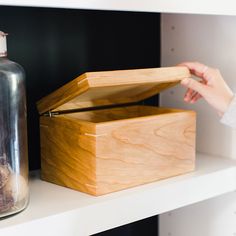 a wooden box sitting on top of a white shelf next to a glass jar and other items