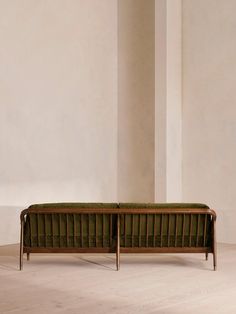 a green couch sitting on top of a wooden floor next to a white wall in an empty room