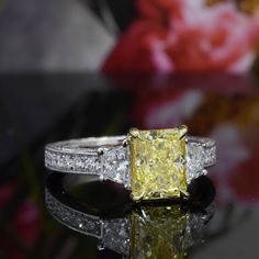 a fancy yellow diamond ring sitting on top of a black surface with flowers in the background