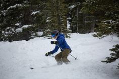 a man riding skis down the side of a snow covered slope with trees in the background