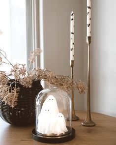 two candles are sitting on a table next to a fake ghost in a glass dome