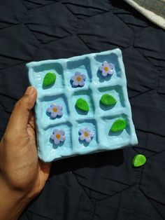 a hand holding a small blue tray with flowers and leaves in it on a black surface