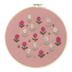 a pink embroidery kit with white and pink flowers on it's side, in the shape of a circle