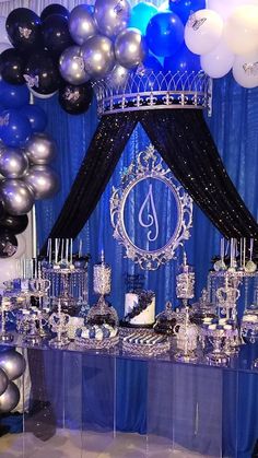 a table topped with lots of silver and black balloons in front of a blue curtain