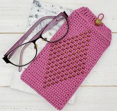 a pink crocheted pouch with eyeglasses on it next to a pair of glasses