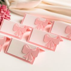 four cards with pink bows on them sitting next to a bouquet of flowers and ribbon