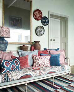 a couch with pillows on it in front of a mirror and vases hanging from the wall