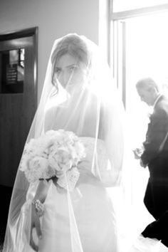 the bride is walking down the aisle with her veil over her head and flowers in her bouquet