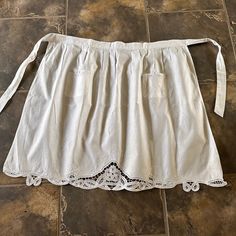 a white skirt with lace on the bottom is laying on a tile floor in front of a stone wall