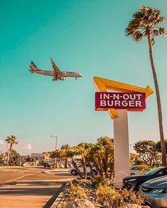 an airplane is flying over the inn - out burger sign in front of palm trees