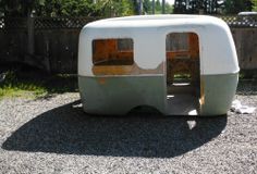 an old camper trailer is sitting in the gravel near a fence and trees,