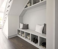 a white room with some shelves filled with shoes and baskets next to a stair case