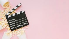 a movie clapper and popcorn on a pink background