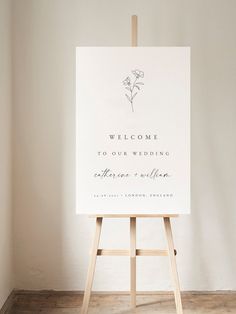 an easel with a welcome sign on it in front of a white wall and wooden floor