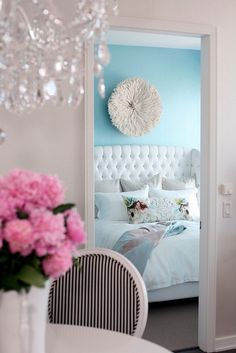 a white bed sitting under a chandelier next to a window with pink flowers