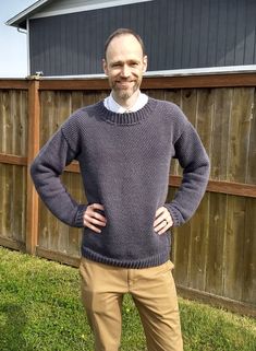 a man standing in front of a fence wearing a sweater and khaki pants