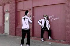 two young men standing in front of a garage door with graffiti on the wall behind them