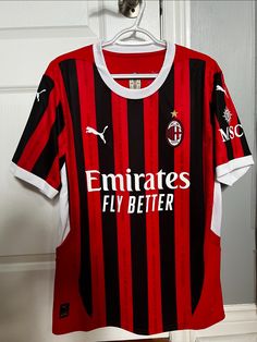 a red and black soccer jersey hanging on a hanger in front of a door