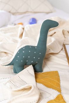 a stuffed dinosaur toy laying on top of a bed next to a pillow and blanket