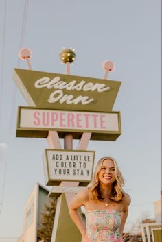 a woman standing in front of a neon sign with her hands on her hips and smiling