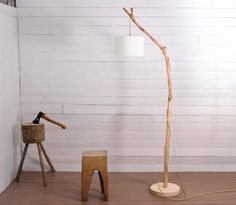 a wooden floor lamp next to a stool and tree branch shaped table lamp in a room with white walls