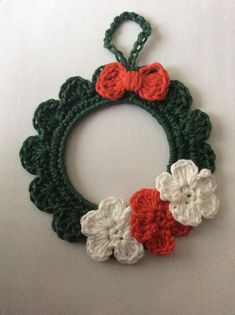 a crocheted wreath with red, white and green flowers hanging on a wall