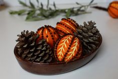 some pine cones are in a bowl with orange and white designs on them, sitting on a table