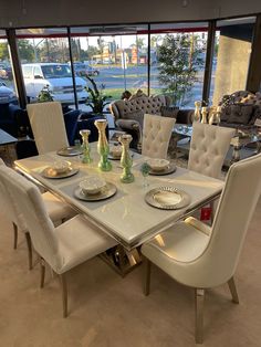 a glass table with white chairs and plates on it