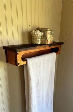 a towel hanging on a wooden shelf above a toilet paper roll and soap dispenser