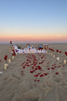 an outdoor ceremony setup on the beach with rose petals and candles in front of it