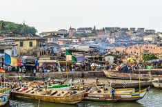 there are many boats that are docked in the water near some buildings and people on the beach