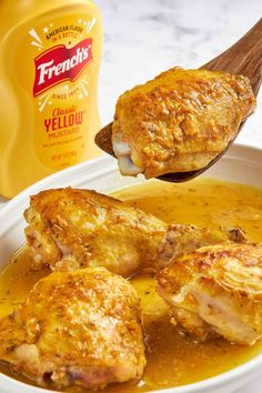 a spoon full of chicken and gravy next to a bottle of mustard