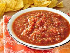 a white bowl filled with lots of red sauce on top of a table next to some tortilla chips