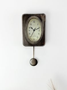 a clock is hanging on the wall next to a potted plant and some feathers