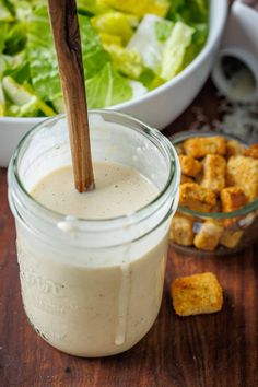 a glass jar filled with dressing next to a bowl of salad and bread cubes