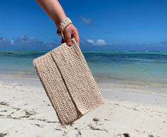 a hand holding a crocheted purse on the beach