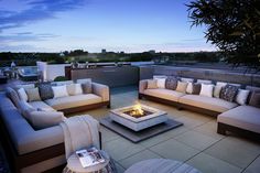 an outdoor living area with couches, tables and fire pit in the evening time