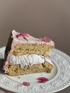 a piece of cake on a plate with pink frosting and rose petals around it