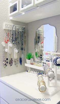 a white counter top sitting under a mirror next to a shelf with jewelry on it