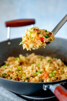 a spoon full of rice and vegetables being lifted from a skillet