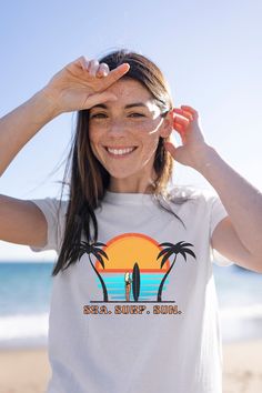 Dive into the summer vibe with our "Sea. Surf. Sun." Women's T-Shirt, your next wardrobe staple for sunny days and beach getaways! Designed for those who carry the spirit of the ocean and the thrill of the surf with them, this vibrant and cheerful tee captures the essence of beach life. 🌊 Product Features: -Unique Design: A striking silhouette of a surfer girl with her board against a backdrop of a stylized sunset and ocean waves, encapsulated by the energizing mantra "Sea. Surf. Sun." -Quality White Beachy Surfing Top, White Beachy Tops For Surfing, White Beachy Top For Surfing, Beachy Tops For Beach Season, Crew Neck Tops For Beach Season Summer Activities, Beachy Surfing Tops For Vacation, Beachy Tops For Surfing Vacation, Summer T-shirt For Beach Season Activities, Beachy Crew Neck T-shirt For Surfing