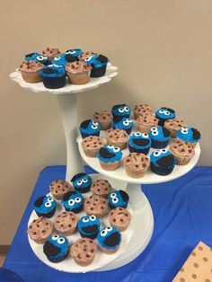 some cupcakes and cookies are sitting on two tiered trays with blue frosting