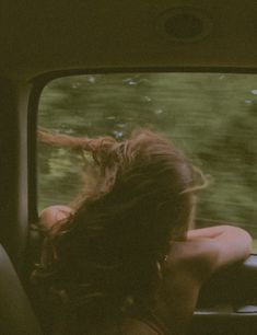 a woman sitting in the passenger seat of a car looking out the window at trees