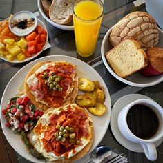 a table topped with plates of food next to cups of coffee and orange juices