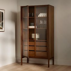 a wooden cabinet with glass doors and drawers in the corner next to a painting on the wall