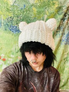 a woman with black hair wearing a white knitted bear hat and nose piercings