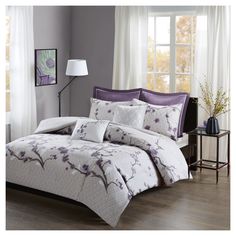 a bed with purple and white comforters in a room next to a window,